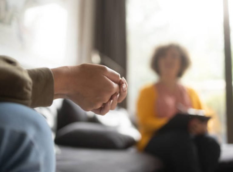 Close-up photo of a teenage girl's hands with fingers crossed nervously. She is in a therapy session with her psychotherapist.